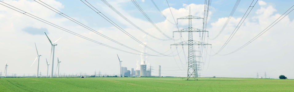 Das Bild zeigt eine Stromtrasse und Windräder in einem grünen Feld - im Hintergrund ein Kraftwerk