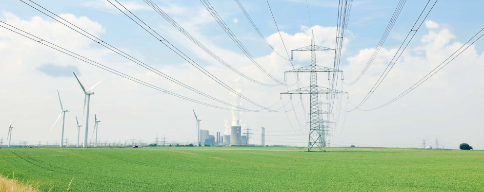 Das Bild zeigt eine Stromtrasse und Windräder in einem grünen Feld - im Hintergrund ein Kraftwerk