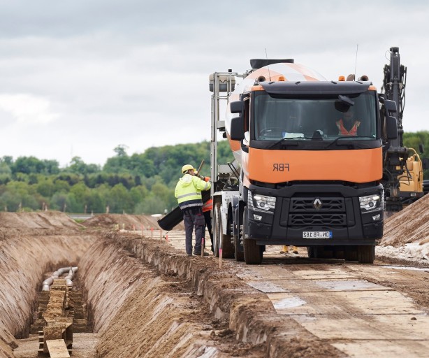 Das Bild zeit einen orangenen LKW neben dem Erdkabelgraben.