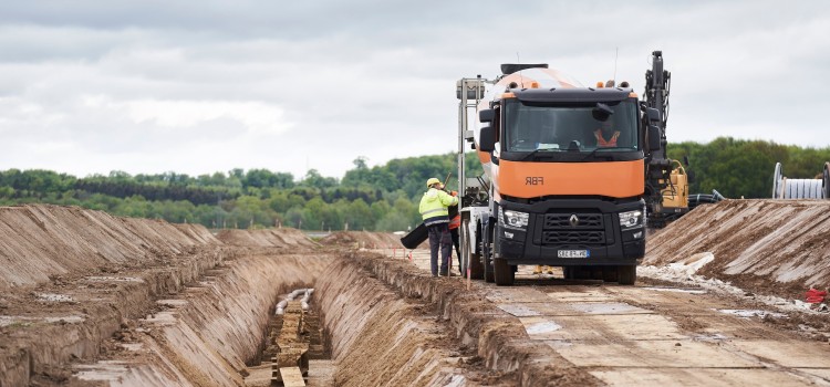 Das Bild zeit einen orangenen LKW neben dem Erdkabelgraben.