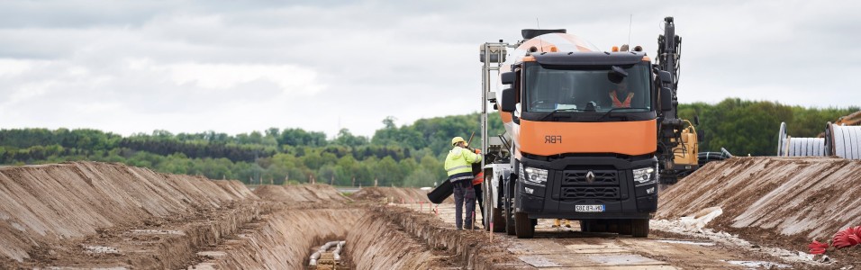 Das Bild zeit einen orangenen LKW neben dem Erdkabelgraben.