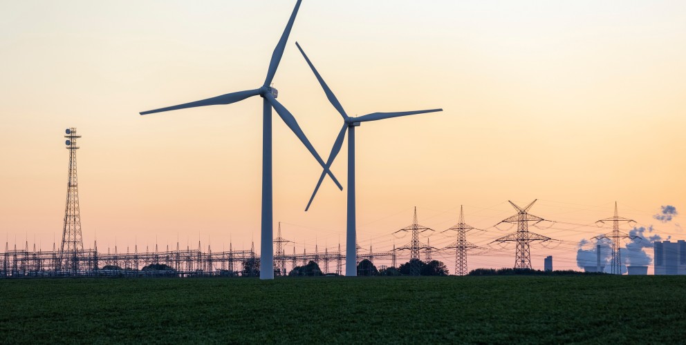 Windräder vor einer Umspannanlage, einem Kraftwerk und Strommasten im Hintergrund