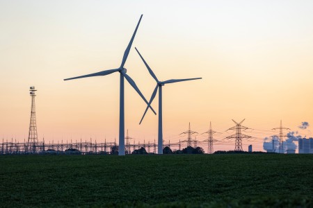 Windräder vor einer Umspannanlage, einem Kraftwerk und Strommasten im Hintergrund
