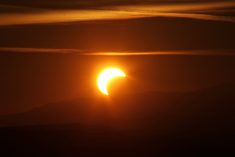 Aufnahme einer Sonnenfinsternis. Der Mond schiebt sich vor die Sonne, das gesamte Bild ist orange eingefärbt. 
