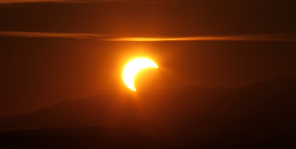 Aufnahme einer Sonnenfinsternis. Der Mond schiebt sich vor die Sonne, das gesamte Bild ist orange eingefärbt. 