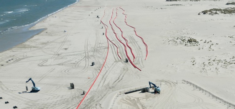 Das Foto zeigt eine Luftaufnahme vom Strand der Insel Norderney, auf dem zwei Bagger und roten Leerrohre für die Stromkabel zu sehen sind.