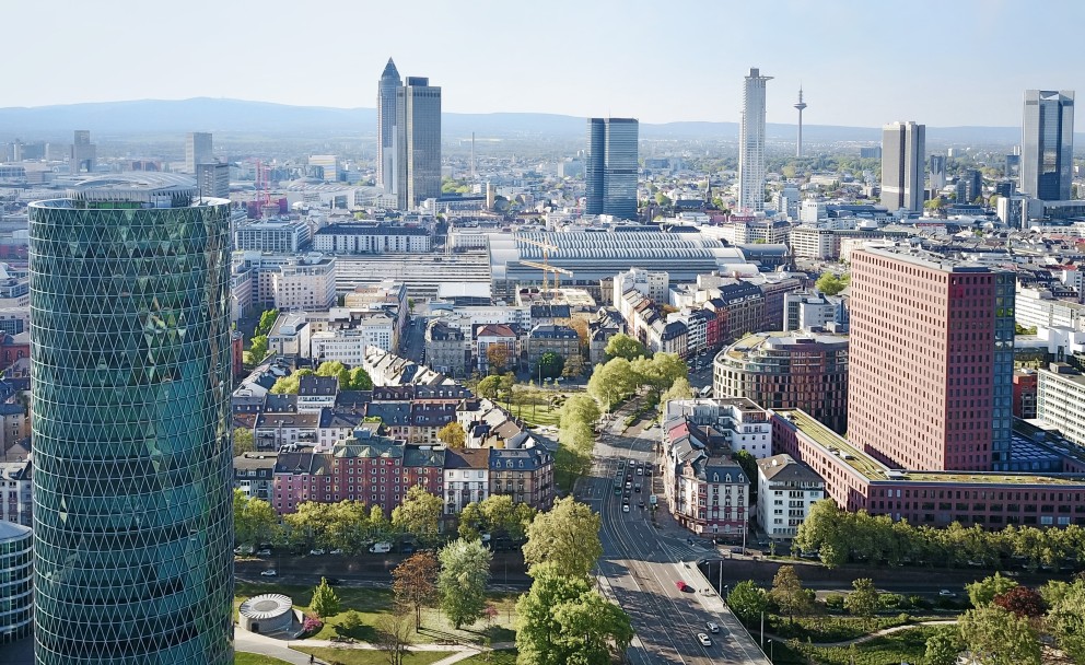Panorama von Frankfurt am Main mit modernen Hochhäusern, darunter der Messeturm und der Europaturm. Im Vordergrund ist das auffällige, grün verglaste Westhafen Tower-Gebäude mit seiner rautenförmigen Glasstruktur zu sehen.
