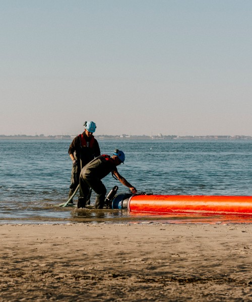 Zwei Monteure am Strand, sie bringen die Muffen an die Rohrleitungen an.
