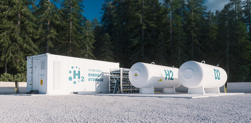 Das Bild zeigt eine Wasserstoffspeicheranlage in einer offenen Umgebung. Links steht ein weißer Container mit der Aufschrift „Hydrogen Energy Storage“ und dem Symbol „H₂“, das auf Wasserstoffspeicherung hinweist. Rechts davon befinden sich zwei weiße, zylindrische Tanks. Der erste Tank ist mit „H₂“ für Wasserstoff beschriftet, während auf dem zweiten Tank „O₂“ steht, was auf Sauerstoff hinweist. Beide Tanks stehen auf stabilen Sockeln. Im Hintergrund ist dichter Wald sichtbar, der auf eine naturnahe Umgebung hindeutet. Die Szene vermittelt Innovation und den Einsatz moderner Technologien für nachhaltige Energie.