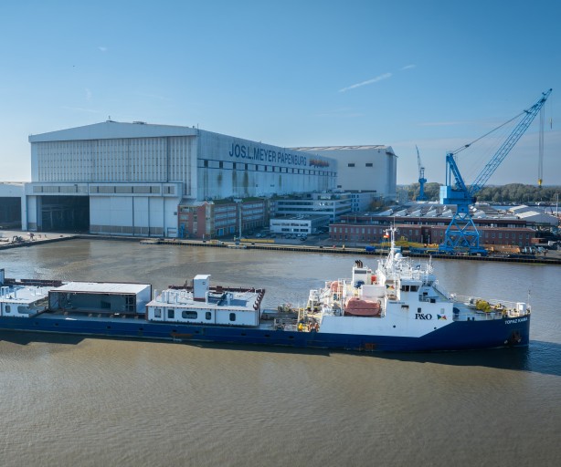 Beladenes Frachtschiff vor Meyer Werft im Wasser vor dem Werftgebäude.