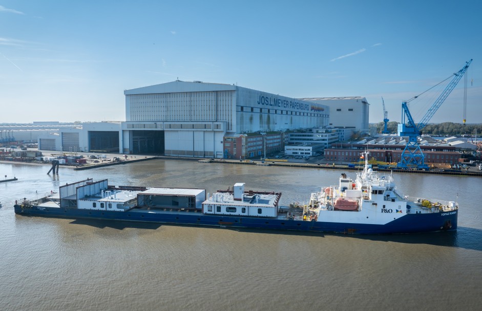 Beladenes Frachtschiff vor Meyer Werft im Wasser vor dem Werftgebäude.