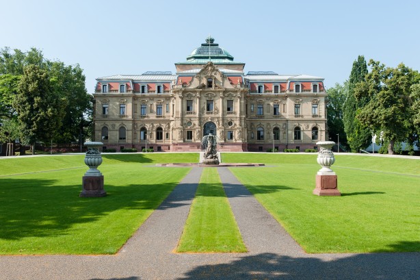 Palais des Bundesverfassungsgerichts vor blauem Himmer. Im Vordergrund eine gepflegte Parkanlage.