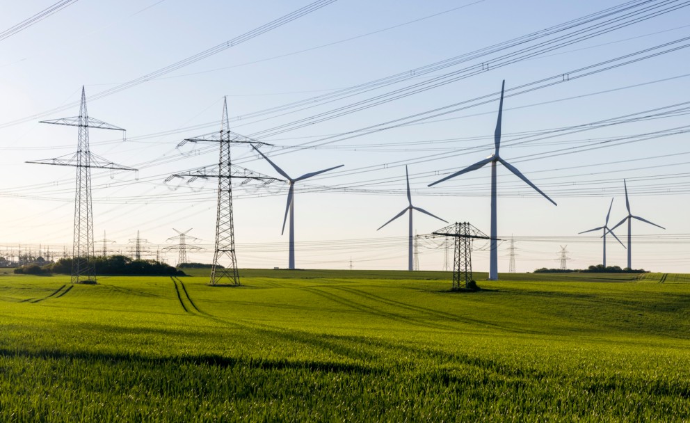 Weitblick auf grünes Feld mit Windrädern, Strommasten und Stromleitungen