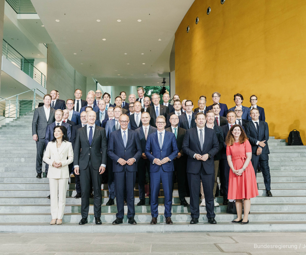 Gruppenfoto der Unternehmsvertreter:innen der Initiative auf einer Treppe in einem modernen repräsentativen Gebäude. Die Personen tragen Geschäftskleidung. Die Treppe ist aus Beton.