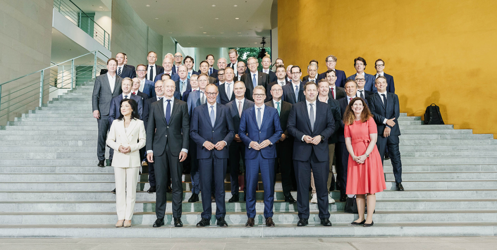 Gruppenfoto der Unternehmsvertreter:innen der Initiative auf einer Treppe in einem modernen repräsentativen Gebäude. Die Personen tragen Geschäftskleidung. Die Treppe ist aus Beton.