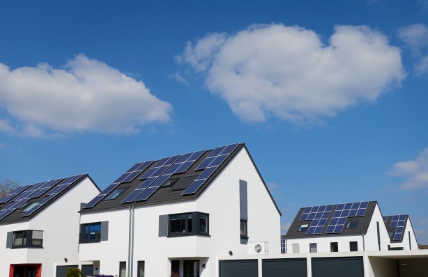 Vier weiße, moderne Einfamilienhäuser mit Solarpanelen auf dem Dach bei sonnigem Wetter.