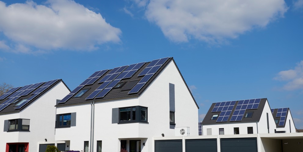 Vier weiße, moderne Einfamilienhäuser mit Solarpanelen auf dem Dach bei sonnigem Wetter.