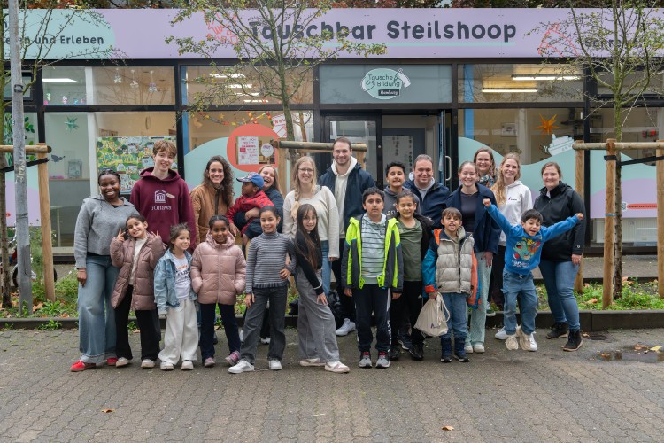 Gruppe von Erwachsenen und Kindern steht vor einem Gebäude mit der Aufschrift 'tauschbar Steilshoop'