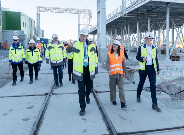 Dr. Christoph Müller, Katherina Reiche und eine gruppe von Personen in Sicherheitsbekleidung laufen auf einer Baustelle.