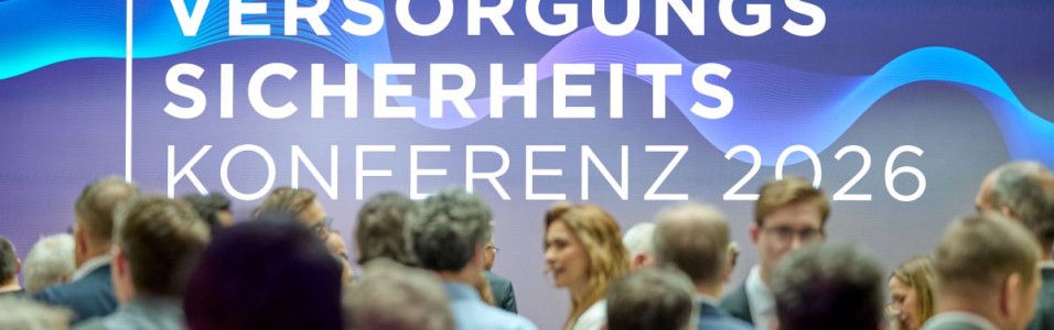Menschenmenge vor einer Wand mit dem Schriftzug VERSORGUNGS SICHERHEITS KONFERENZ 2026
