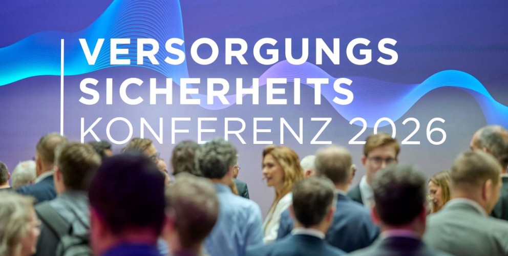 Menschenmenge vor einer Wand mit dem Schriftzug VERSORGUNGS SICHERHEITS KONFERENZ 2026