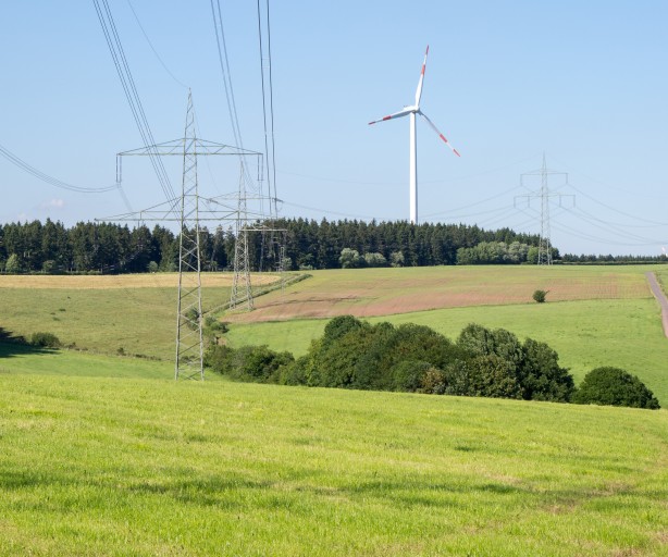 Das Bild zeigt eine Trasse in hügeliger Landschaft. Windräder sind am Horizont zu sehen.