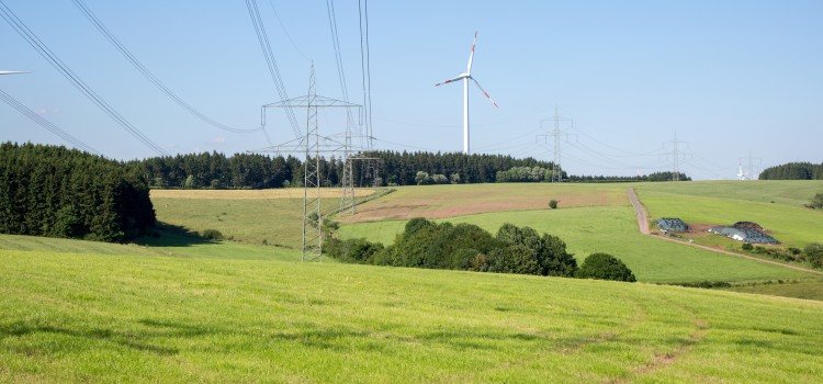 Das Bild zeigt eine Trasse in hügeliger Landschaft. Windräder sind am Horizont zu sehen.