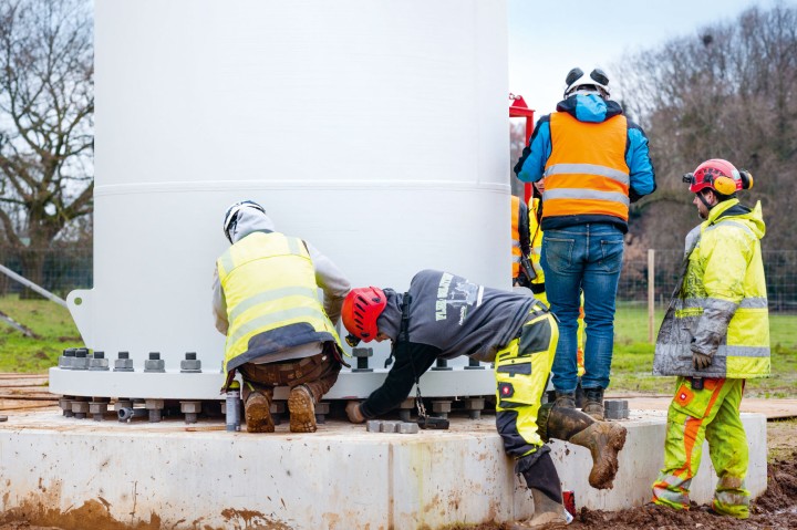 Der Mastschaft im Fundament. Davor Menschen in Schutzkleidung.