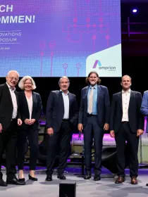 Das Bild zeigt sechs Personen auf einer Bühne beim Innovationssymposium 2023 von Amprion, das am 25. August 2023 in der Zeche Zollverein, Essen, stattfand.
Details:
Hinter der Gruppe befindet sich eine große digitale Leinwand mit der Aufschrift:
 