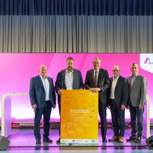 Fünf Männer in Anzügen stehen auf einer Bühne und halten gemeinsam ein gelbes Plakat mit Unterschriften, das die neue Rahmenregelung für Erdkabelprojekte 2025 zeigt. Der Hintergrund ist magentafarben mit Amprion-Logo.