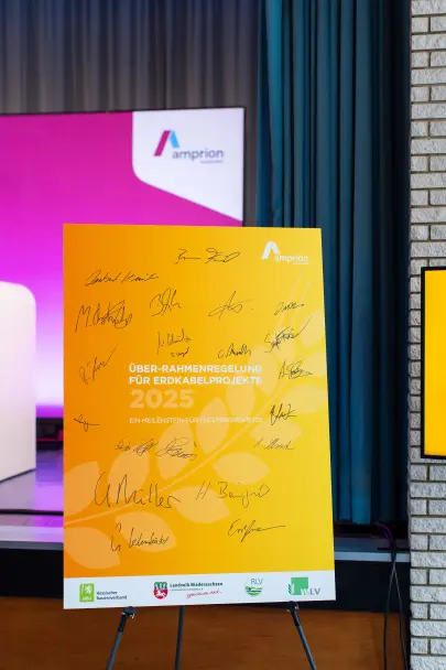Detailaufnahme des gelben Plakats mit der Aufschrift „Über-Rahmenregelung für Erdkabelprojekte 2025 – Ein Meilenstein für die Energiewende“. Mehrere Unterschriften sind deutlich zu erkennen. Unten Logos landwirtschaftlicher Verbände sowie das Amprion-Logo.