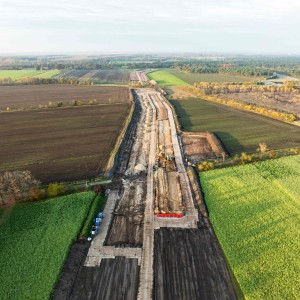 Luftaufnahme einer Baustelle für eine Erdkabel-Trasse, die sich als breiter, dunkler Erdstreifen durch eine Landschaft aus grünen und braunen Feldern zieht.