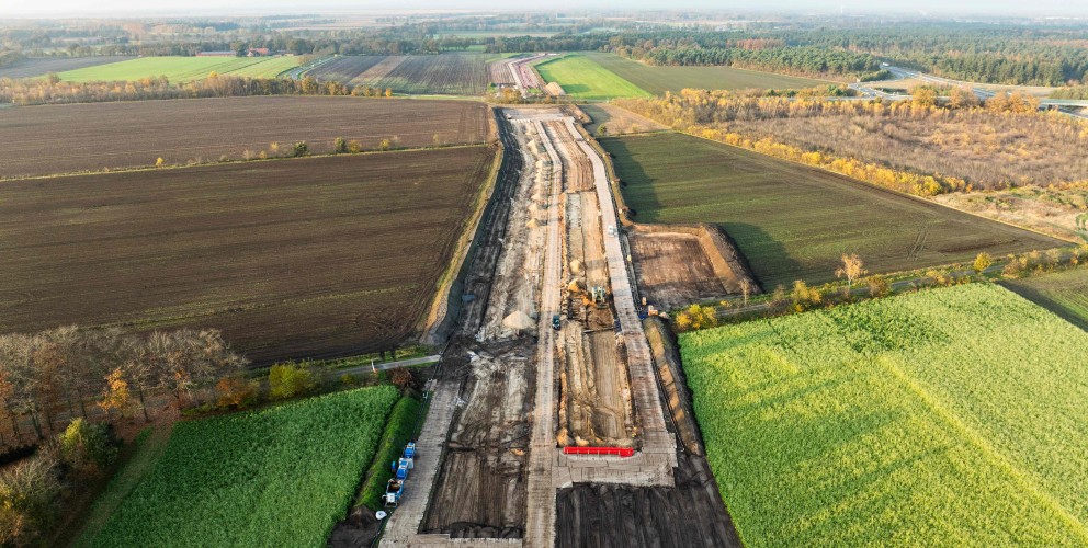 Luftaufnahme einer Baustelle für eine Erdkabel-Trasse, die sich als breiter, dunkler Erdstreifen durch eine Landschaft aus grünen und braunen Feldern zieht.