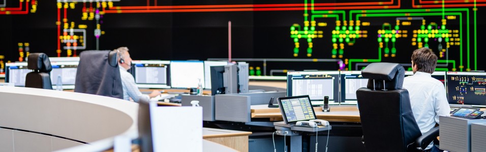 Das Bild zeigt einen Ausschnitt der Hauptschaltleitung der Amprion GmbH. Im Hintergrund Das große Rückmeldebild, im Vordergrund Schalt-Ingenieure an ihren Arbeitsplätzen.