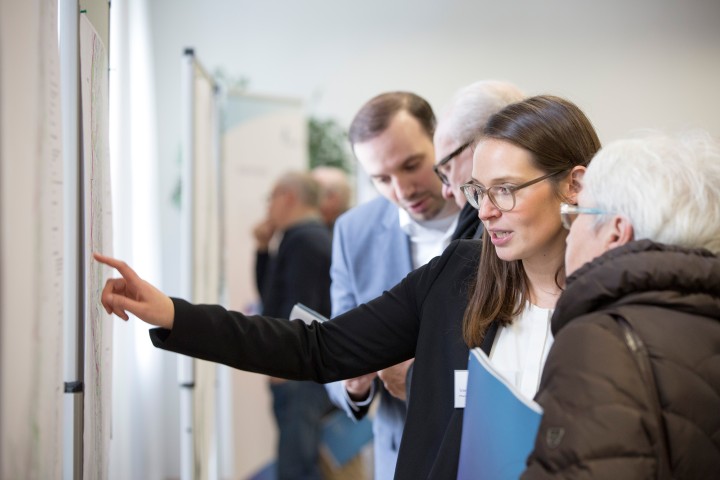 Das helle Bild zeigt zwei Amprion Mitarbeiter, die Bürgern an Stellwänden die Planungen im Projekt A-Nord erläutern.