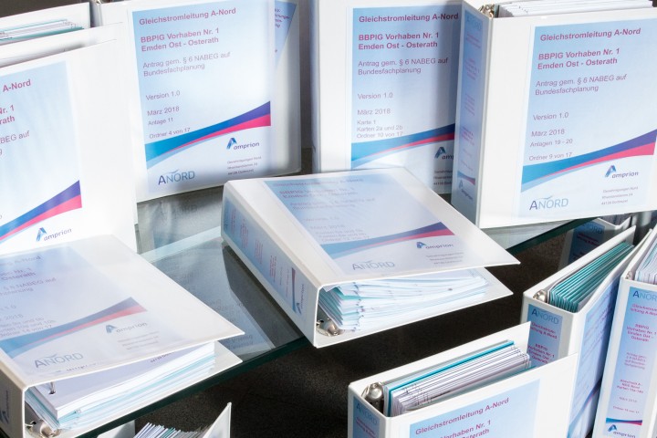 Das helle Bild im Querformat zeigt neun weiße Ordner auf einem Glastisch.