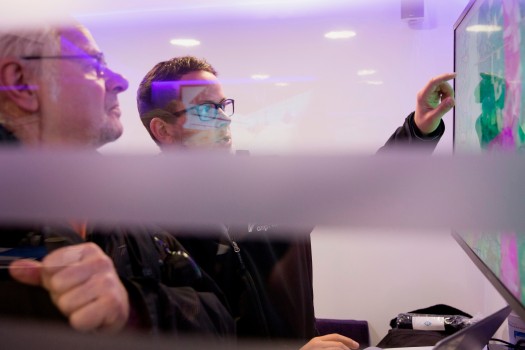 Das leicht lilafarbene Bild zeigt einen Amprion-Mitarbeiter, der einem Bürger an einem Bildschirm die Trassenkorridore im Projekt A-Nord erläutert.