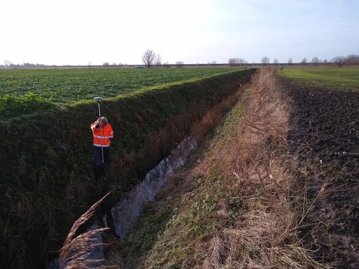 Mann  mit langem Messstab im Graben inmitten einer Feldlandschaft
(c) Freigang und Schumann