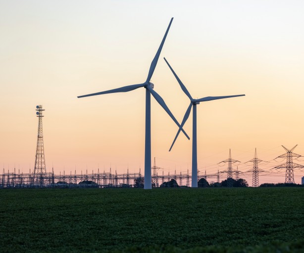 Windräder vor einer Umspannanlage, einem Kraftwerk und Strommasten im Hintergrund