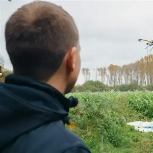 Ein Mann beobachtet den Flug einer Drohne über einem bewachsenen Feld, im Einsatz zur Kampfmittelerkundung vor Baubeginn.