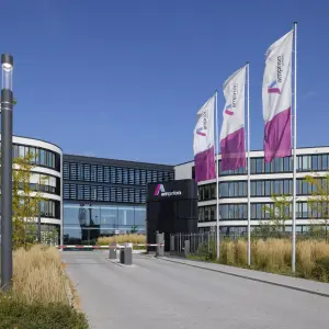 Hauptsitz von Amprion mit geschwungener Fassade, Glasfront und wehenden Unternehmensflaggen vor blauem Himmel.