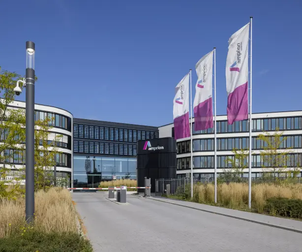 Hauptsitz von Amprion mit geschwungener Fassade, Glasfront und wehenden Unternehmensflaggen vor blauem Himmel.