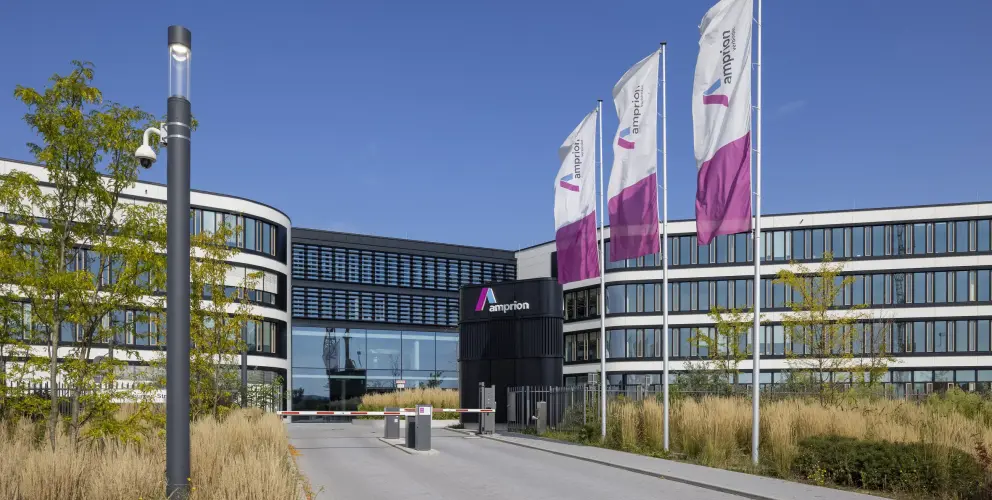 Hauptsitz von Amprion mit geschwungener Fassade, Glasfront und wehenden Unternehmensflaggen vor blauem Himmel.