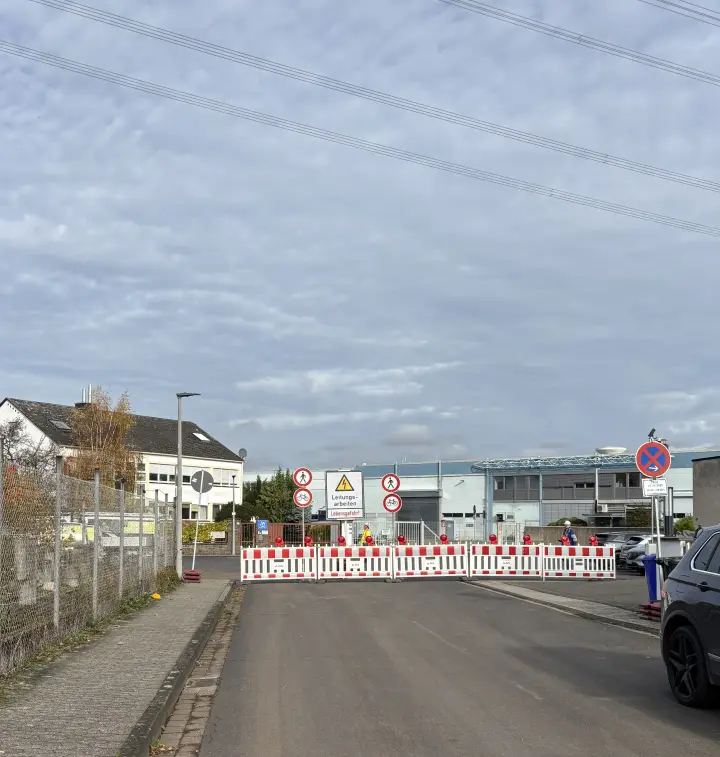 Eine Straße ist mit Absperrbaken und Baustellenhinweisen für Leitungsarbeiten gesperrt; Schilder informieren über Durchgangsverbot.