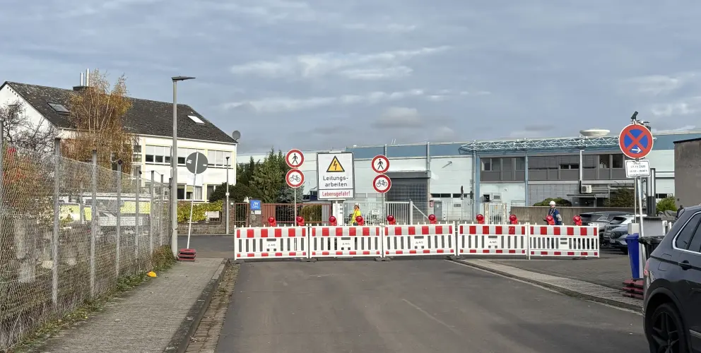 Eine Straße ist mit Absperrbaken und Baustellenhinweisen für Leitungsarbeiten gesperrt; Schilder informieren über Durchgangsverbot.