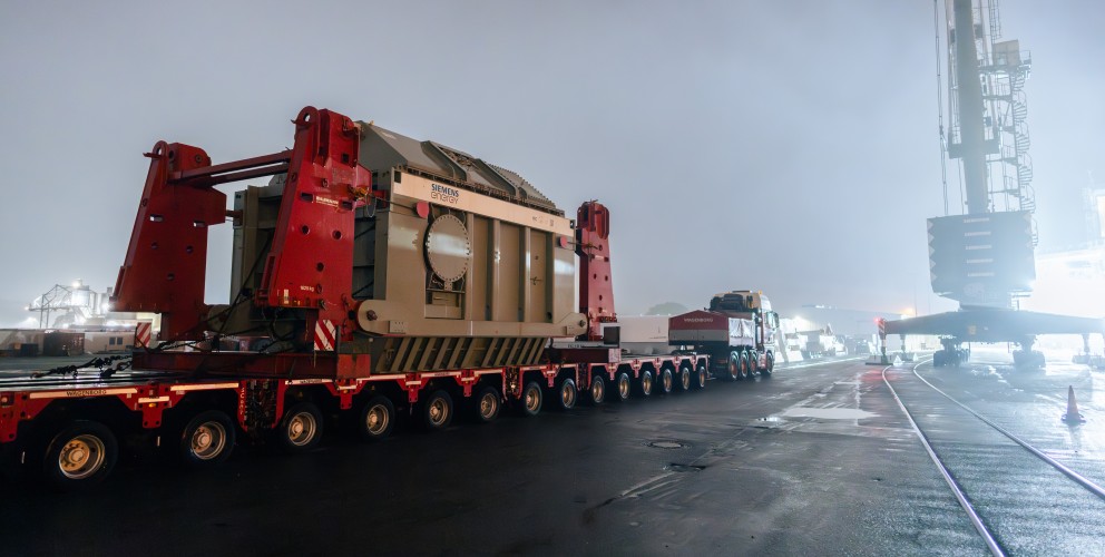 Ein Schwerlasttransport bringt einen großen Siemens-Energy-Transformator bei Nacht auf einem Hafengelände ans Ziel.