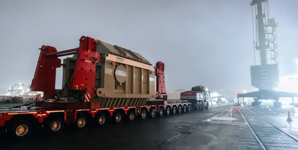 Ein Schwerlasttransport bringt einen großen Siemens-Energy-Transformator bei Nacht auf einem Hafengelände ans Ziel.
