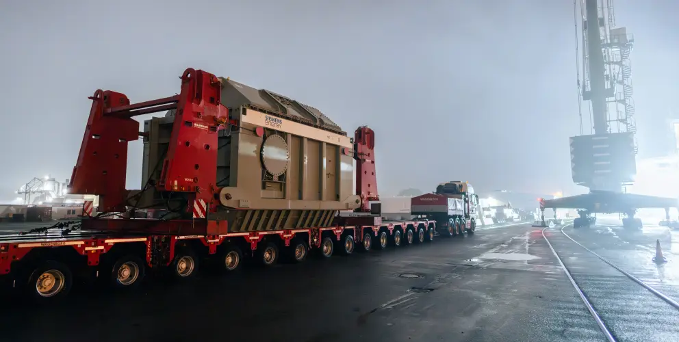 Ein Schwerlasttransport bringt einen großen Siemens-Energy-Transformator bei Nacht auf einem Hafengelände ans Ziel.