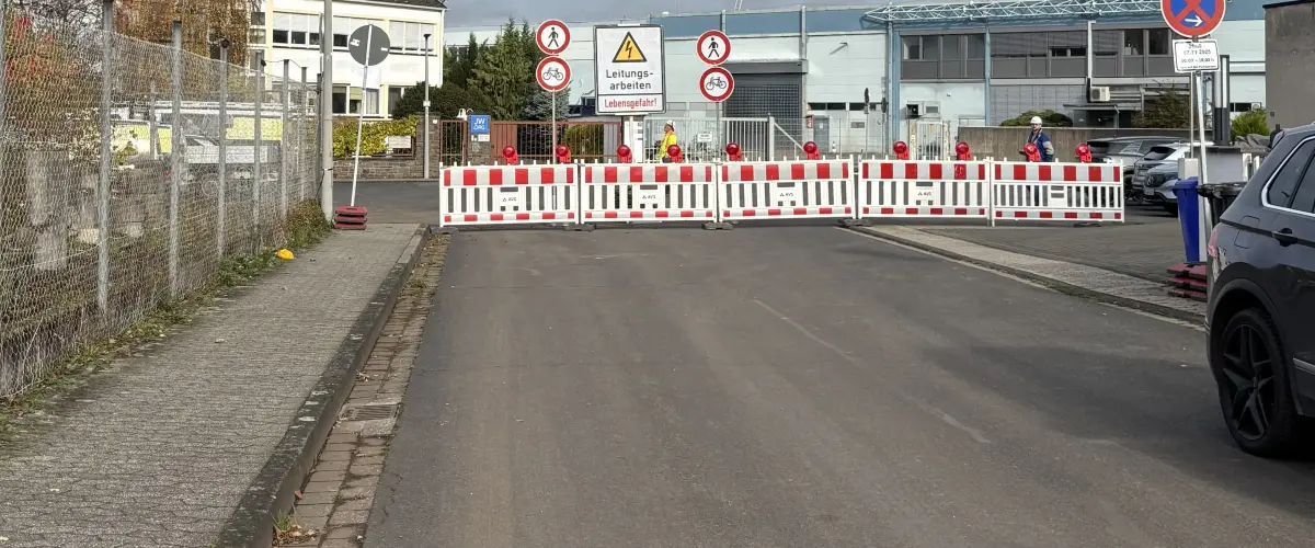 Eine Straße ist mit Absperrbaken und Baustellenhinweisen für Leitungsarbeiten gesperrt; Schilder informieren über Durchgangsverbot.
