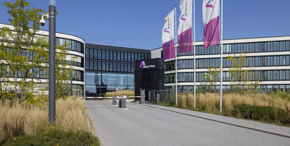 Hauptsitz von Amprion mit geschwungener Fassade, Glasfront und wehenden Unternehmensflaggen vor blauem Himmel.